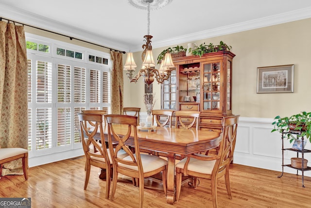 dining area featuring a chandelier, ornamental molding, light wood finished floors, and wainscoting