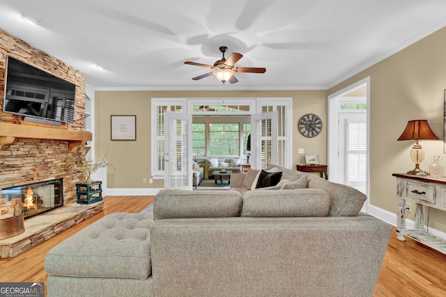 living room with a stone fireplace, crown molding, a ceiling fan, healthy amount of natural light, and wood finished floors
