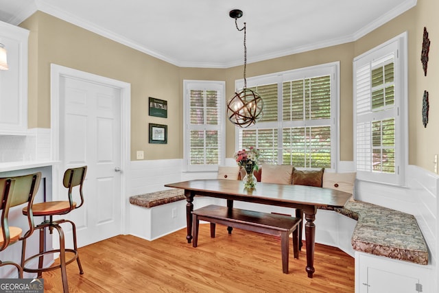 dining room with breakfast area, light wood-type flooring, ornamental molding, a wainscoted wall, and a chandelier