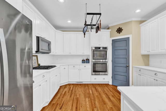 kitchen with stainless steel appliances, backsplash, ornamental molding, light wood-style floors, and white cabinetry