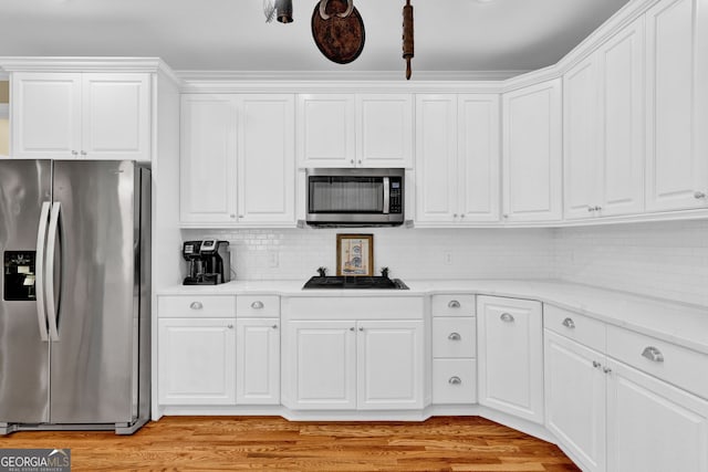 kitchen with appliances with stainless steel finishes, backsplash, white cabinetry, light wood finished floors, and light stone countertops
