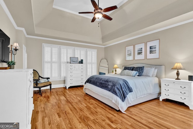 bedroom with a raised ceiling, light wood-style flooring, ornamental molding, and a ceiling fan