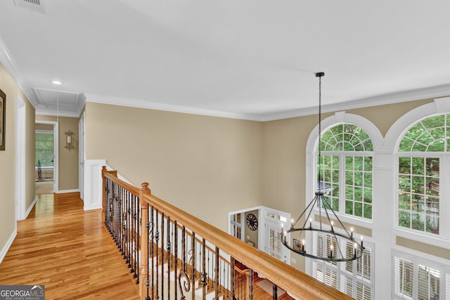 hall featuring attic access, an upstairs landing, a chandelier, light wood-style floors, and crown molding