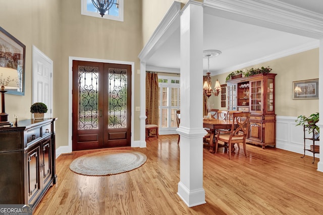 foyer with a chandelier, light wood-type flooring, french doors, wainscoting, and ornamental molding