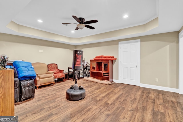 living area featuring a raised ceiling, wood finished floors, a ceiling fan, recessed lighting, and baseboards