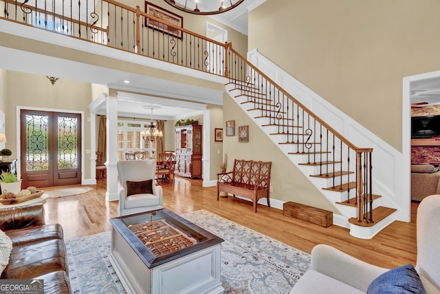 living room featuring a chandelier, a high ceiling, stairs, wood finished floors, and french doors