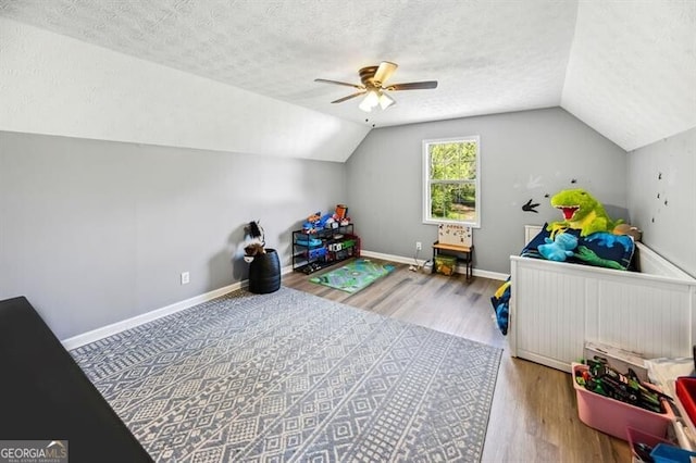 recreation room featuring vaulted ceiling, wood finished floors, ceiling fan, a textured ceiling, and baseboards