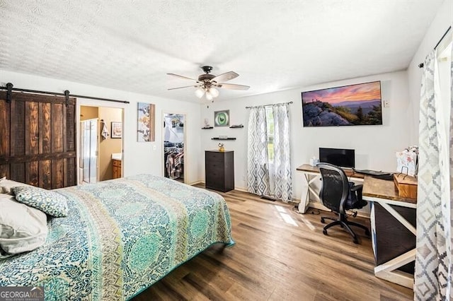 bedroom featuring wood finished floors, a barn door, an office area, a ceiling fan, and a textured ceiling