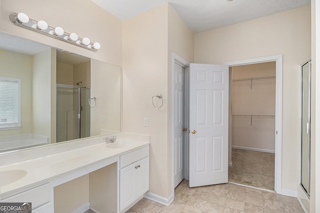 bathroom featuring a stall shower, a spacious closet, double vanity, a garden tub, and baseboards
