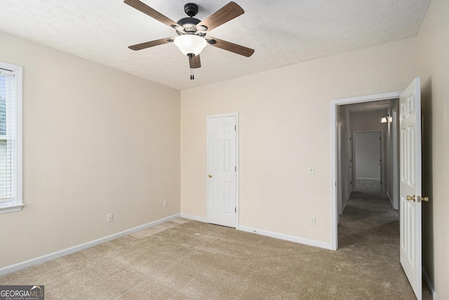 unfurnished bedroom featuring light colored carpet, baseboards, multiple windows, and a ceiling fan