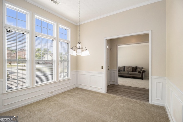 unfurnished dining area with carpet, a chandelier, ornamental molding, a decorative wall, and a wainscoted wall