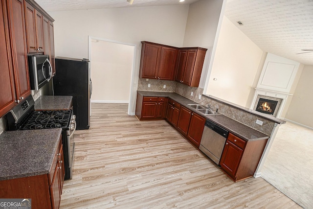 kitchen featuring stainless steel appliances, vaulted ceiling, a sink, light wood-style flooring, and a textured ceiling