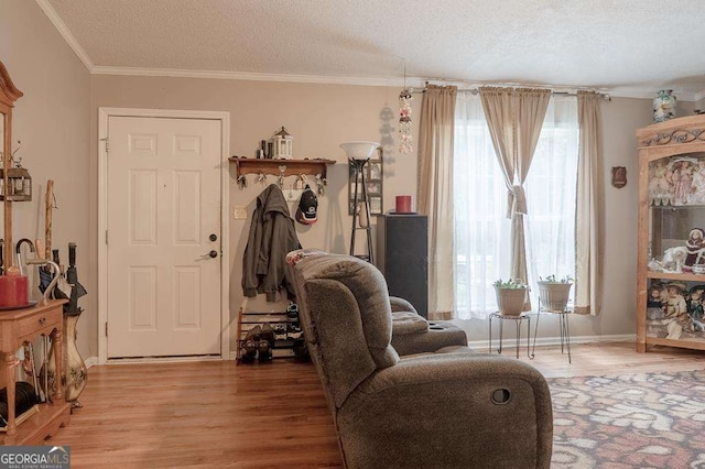 living area featuring wood finished floors, a textured ceiling, ornamental molding, and baseboards