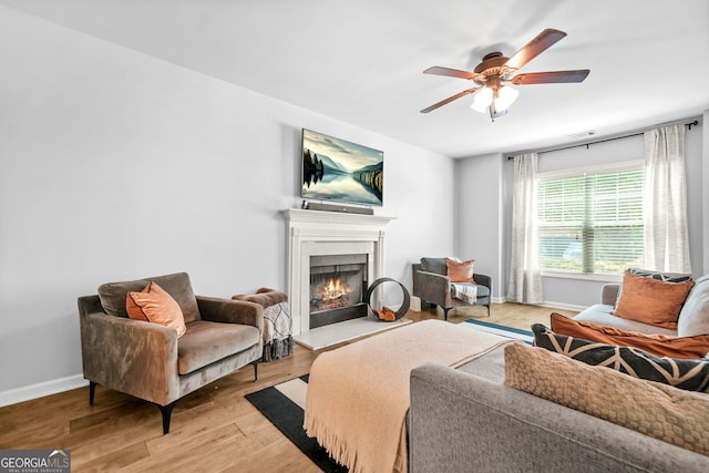 1326 Castleberry Dr, Buford, GA 30518 - living room with a warm lit fireplace, ceiling fan, baseboards, and light wood-type flooring