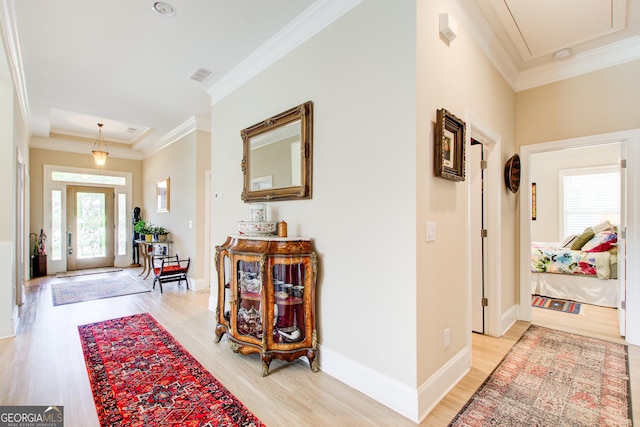 foyer entrance featuring light wood finished floors, ornamental molding, baseboards, and a raised ceiling