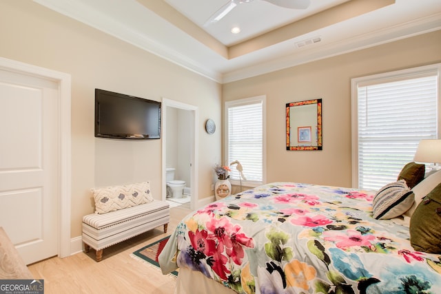 bedroom with light wood-style flooring, crown molding, a raised ceiling, ensuite bath, and a ceiling fan