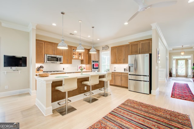 kitchen featuring stainless steel appliances, light wood-style floors, light countertops, crown molding, and a kitchen breakfast bar