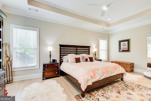 bedroom featuring crown molding, light wood finished floors, a raised ceiling, baseboards, and ceiling fan