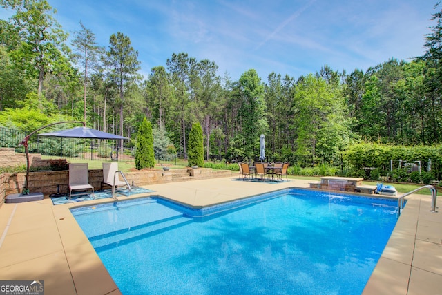 outdoor pool featuring a patio area, fence, a hot tub, and a wooded view