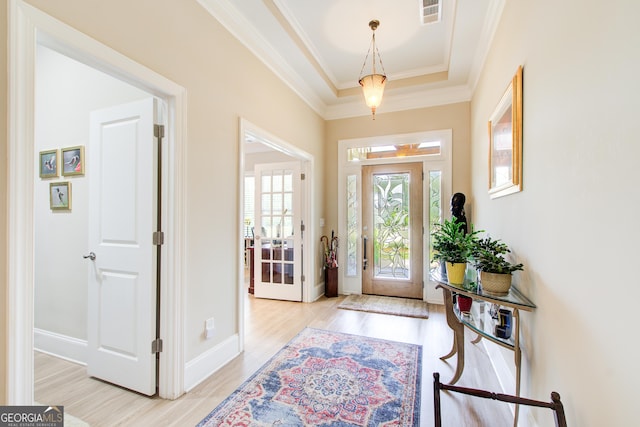 entrance foyer with light wood-style flooring, crown molding, a tray ceiling, and baseboards