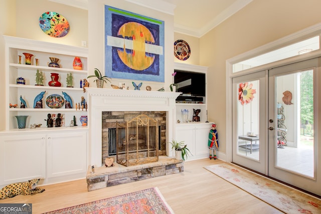 living room featuring french doors, wood finished floors, crown molding, and a stone fireplace