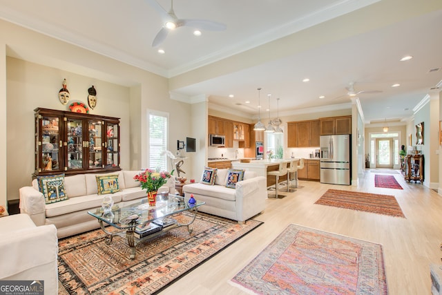 living area featuring ceiling fan, healthy amount of natural light, light wood-style flooring, ornamental molding, and recessed lighting