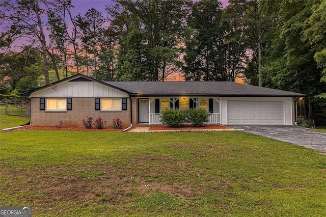 ranch-style home with a garage, asphalt driveway, a porch, a front yard, and brick siding