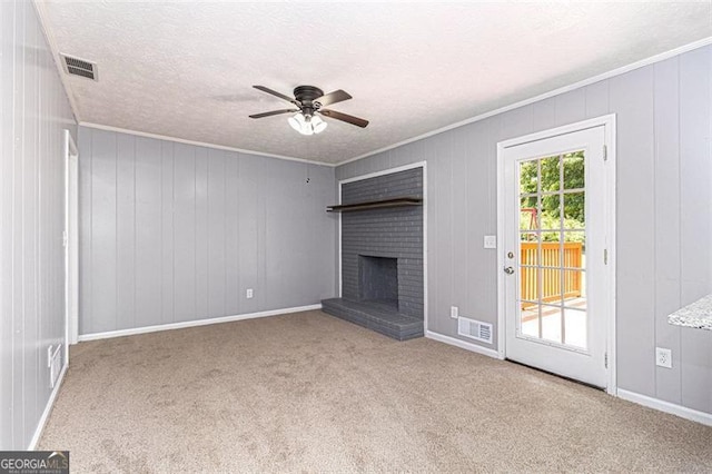 unfurnished living room featuring a ceiling fan, ornamental molding, carpet floors, a brick fireplace, and a textured ceiling