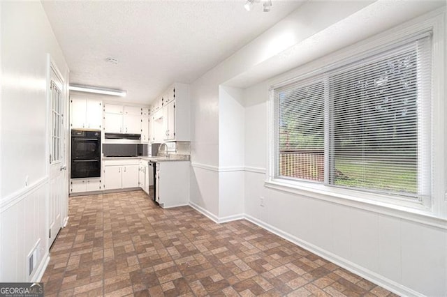 kitchen featuring brick patterned floors, white cabinetry, light countertops, under cabinet range hood, and dishwashing machine
