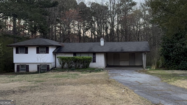 tri-level home featuring asphalt driveway, a chimney, an attached carport, brick siding, and a front yard
