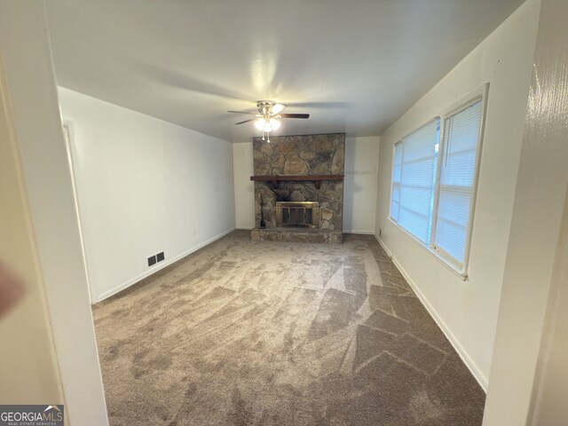 unfurnished living room featuring carpet, ceiling fan, a stone fireplace, and baseboards