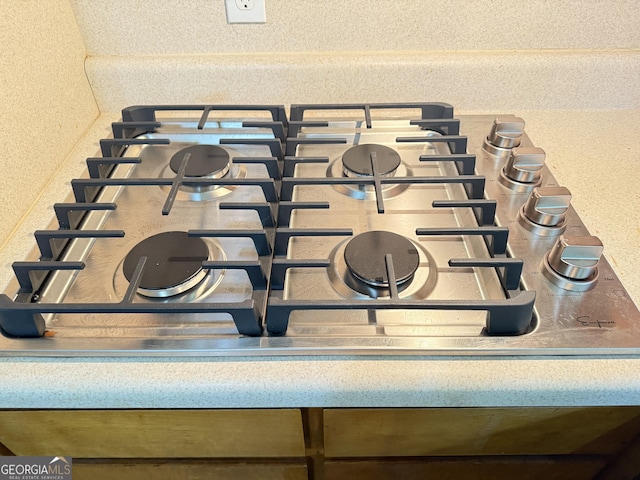 kitchen view of a textured wall and stainless steel gas cooktop