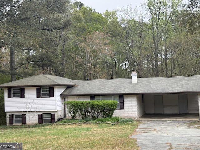tri-level home with brick siding, asphalt driveway, a chimney, an attached carport, and a front lawn