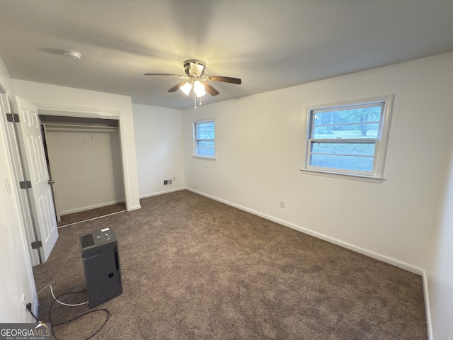 unfurnished bedroom featuring dark carpet, baseboards, a closet, and a ceiling fan