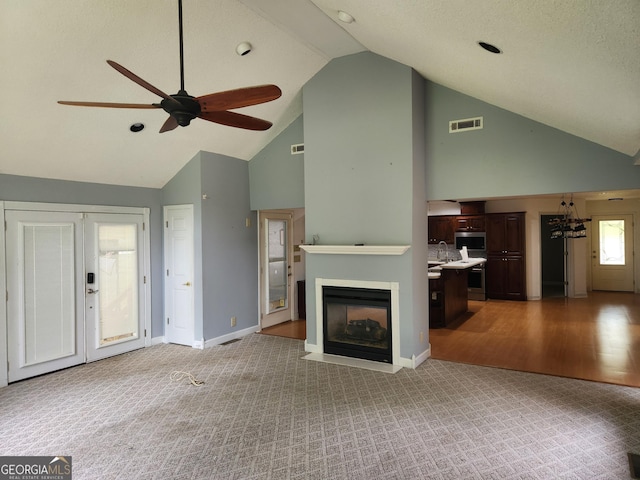 unfurnished living room with high vaulted ceiling, ceiling fan, carpet, a fireplace with flush hearth, and baseboards