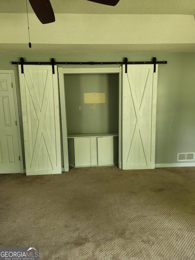 unfurnished bedroom with a barn door, carpet flooring, baseboards, and ceiling fan