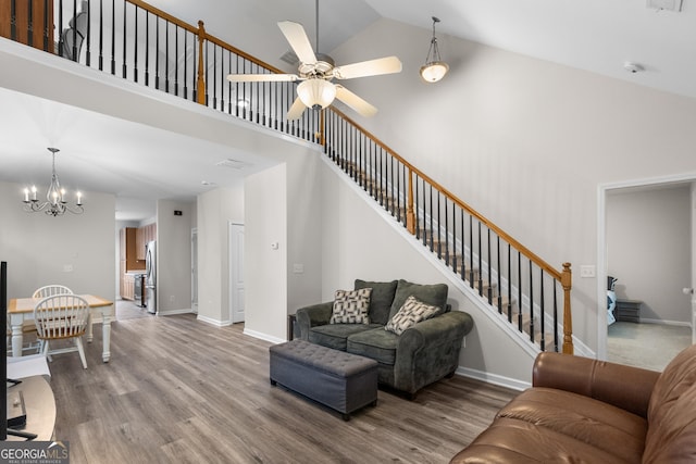 living room with a ceiling fan, a chandelier, wood finished floors, stairs, and high vaulted ceiling