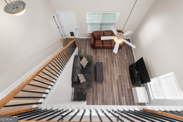 living room with wood finished floors, stairs, a ceiling fan, baseboards, and a towering ceiling