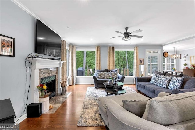living room with crown molding, ceiling fan, a fireplace, wood finished floors, and a chandelier