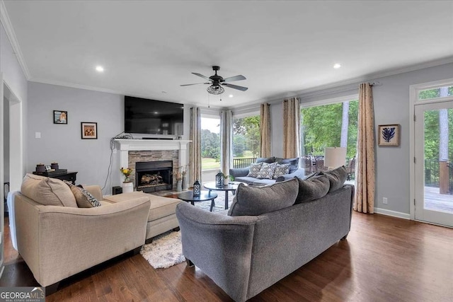 living area with crown molding, dark wood-style floors, a stone fireplace, a ceiling fan, and recessed lighting