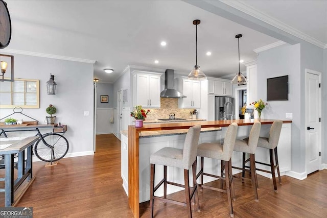 kitchen with wall chimney exhaust hood, ornamental molding, appliances with stainless steel finishes, backsplash, and white cabinetry