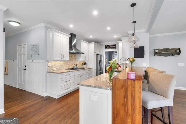 kitchen with wall chimney exhaust hood, stainless steel appliances, dark wood-style flooring, crown molding, and a breakfast bar