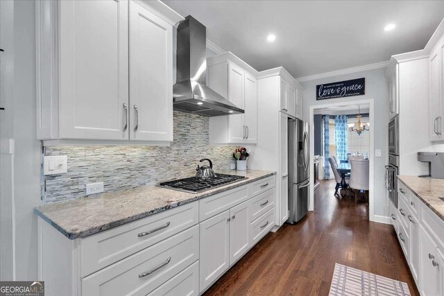 kitchen featuring wall chimney exhaust hood, stainless steel appliances, backsplash, white cabinetry, and ornamental molding