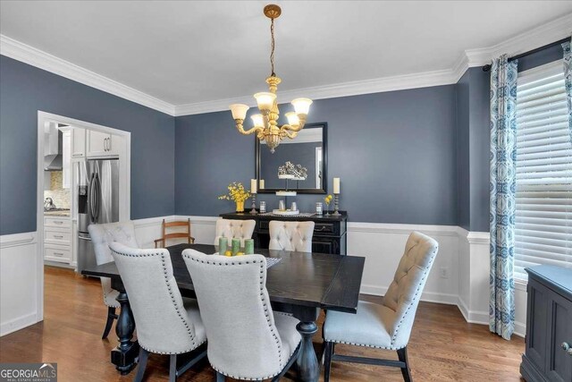 dining room featuring a chandelier, wood finished floors, healthy amount of natural light, ornamental molding, and a wainscoted wall