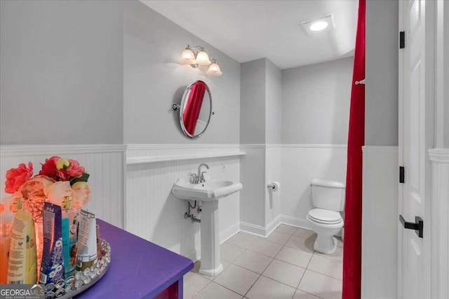half bath with wainscoting, tile patterned floors, toilet, and a sink