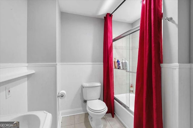 bathroom featuring tile patterned floors, toilet, combined bath / shower with glass door, and a wainscoted wall