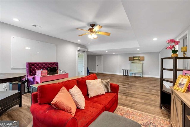 living room with a wall mounted air conditioner, ceiling fan, wood finished floors, baseboards, and recessed lighting