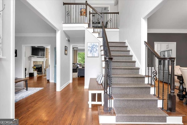 foyer entrance featuring stairway, wood finished floors, a fireplace, ornamental molding, and a towering ceiling