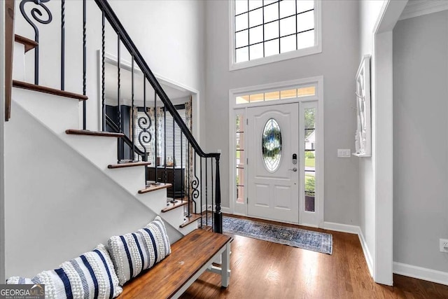 foyer entrance featuring wood finished floors, a high ceiling, baseboards, and stairs
