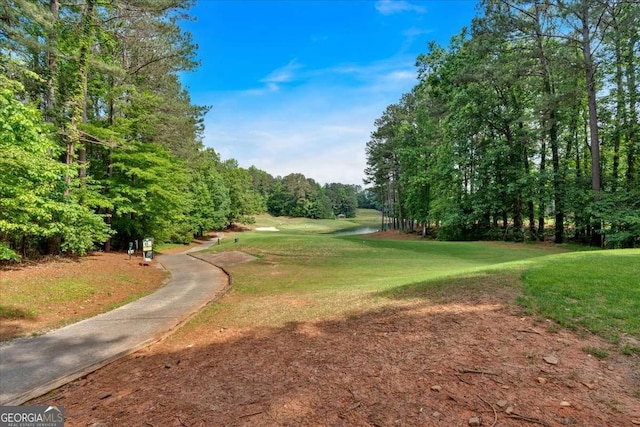 view of home's community with golf course view, a lawn, and view of wooded area